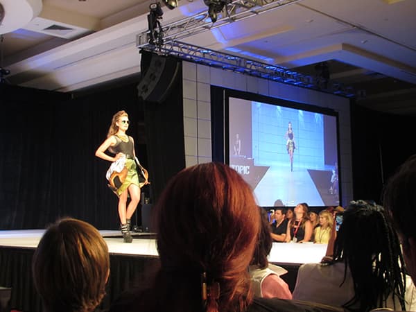 Her Universe Fashion Show logo with silhouettes of models on a runway